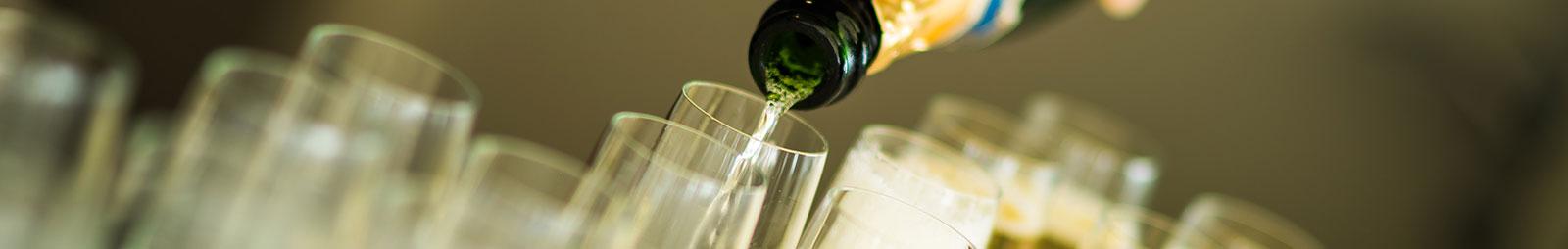 A bottle pours its contents out into several waiting champagne flutes.